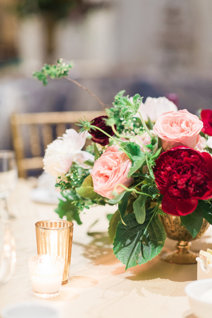 Garden-style centerpiece in gold compote. Red peonies, coral roses, spirea.