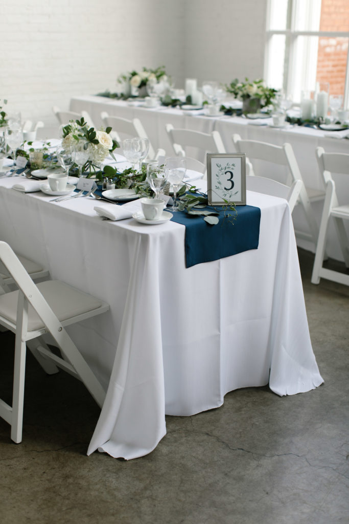 white, sage, and navy wedding centerpieces on long, rectangular tables