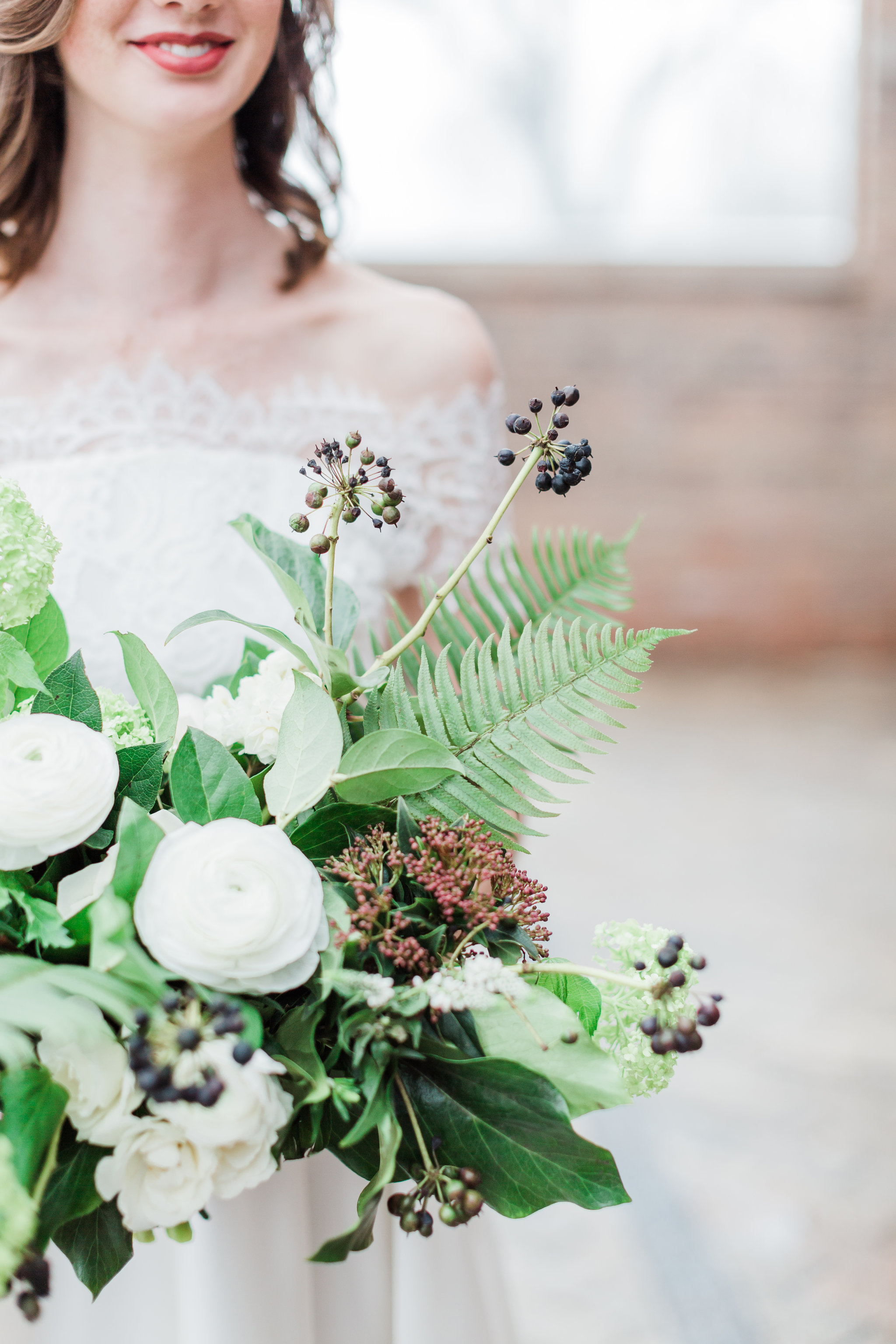 Neutral colored winter wedding bouquet in white, green, and navy. With ranunculus, spray roses, fern, and berries.