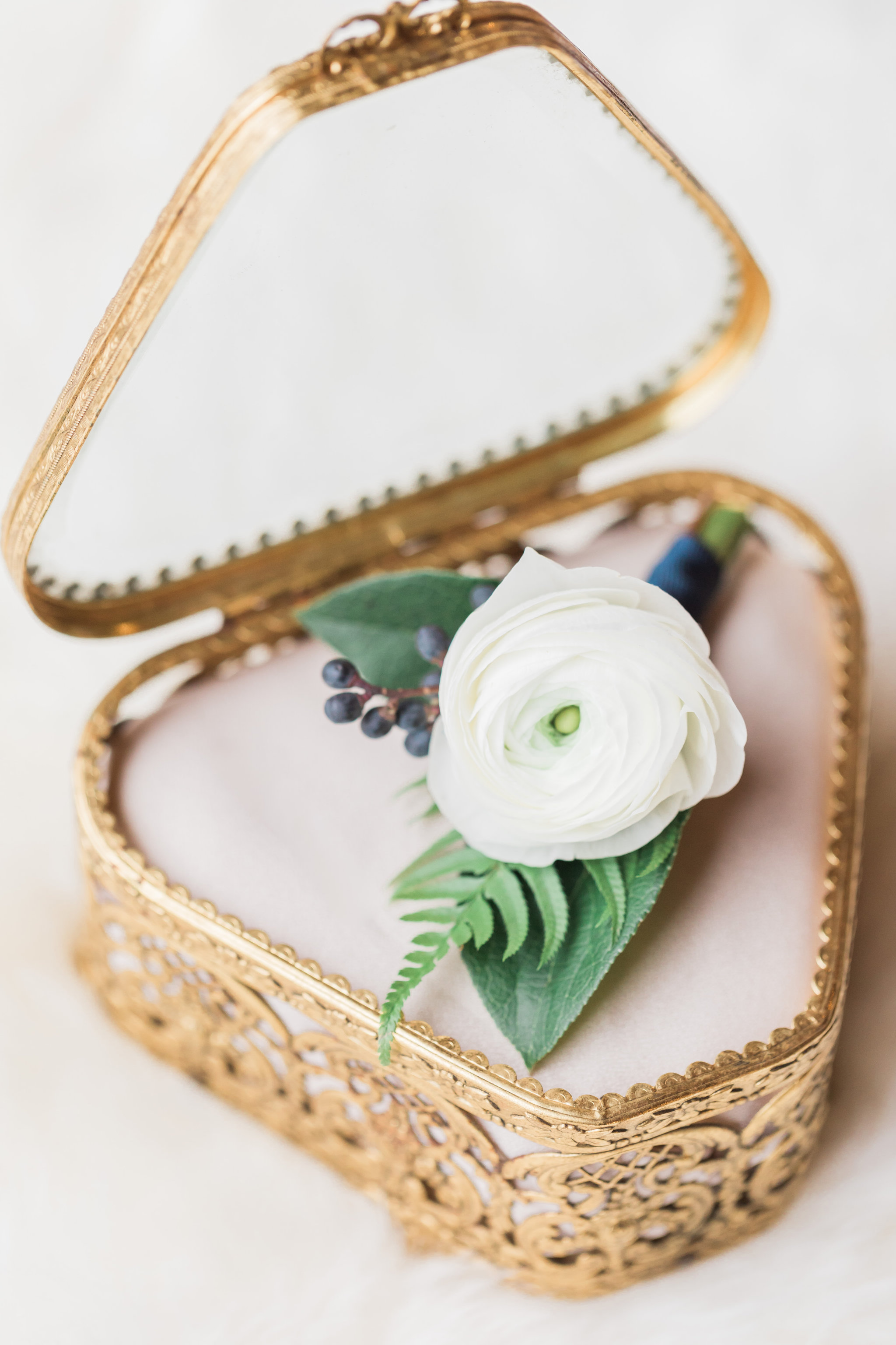 Gold ring box with white ranunculus boutonniere, navy berries, fern.