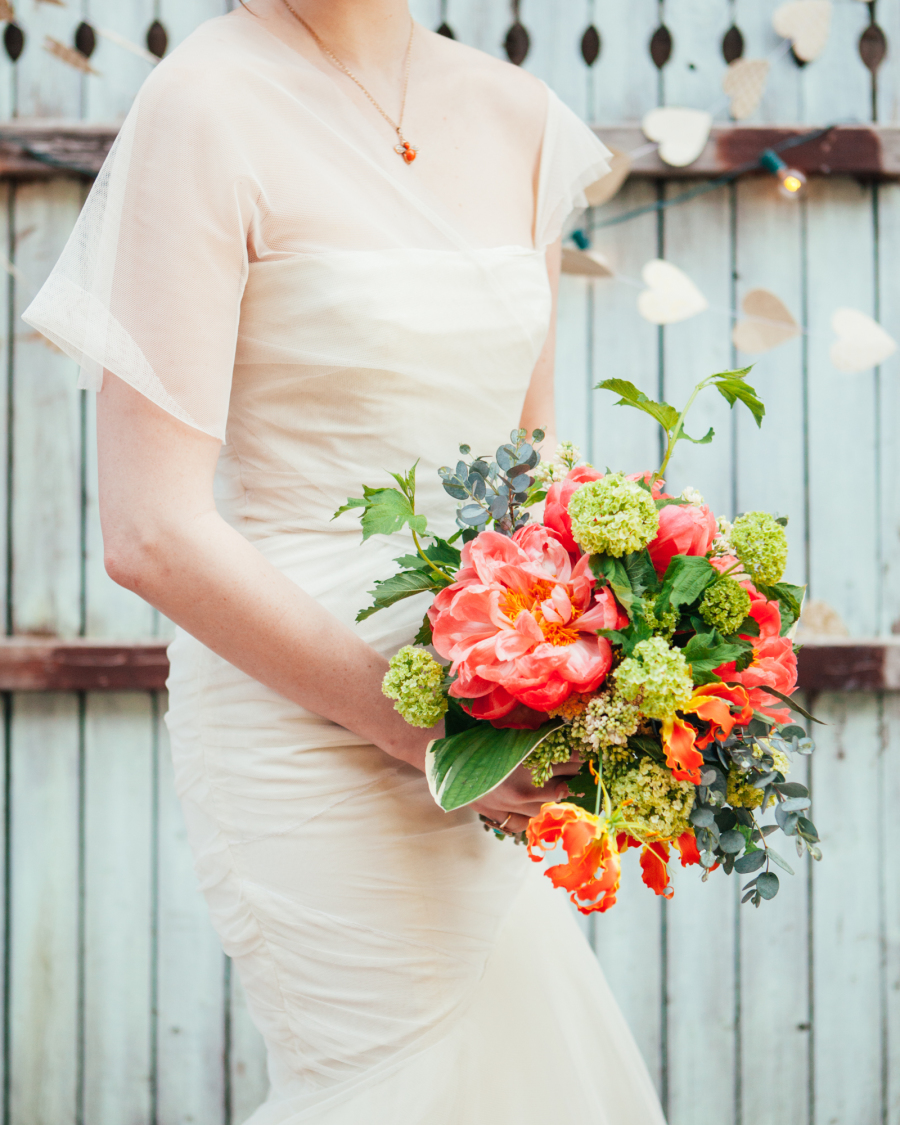 Bride holding bright garden-style bouquet with peonies and viburnum.