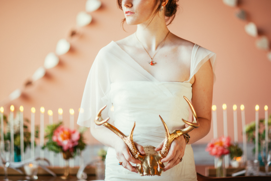 Bride in draping wedding gown holding gold antlers.