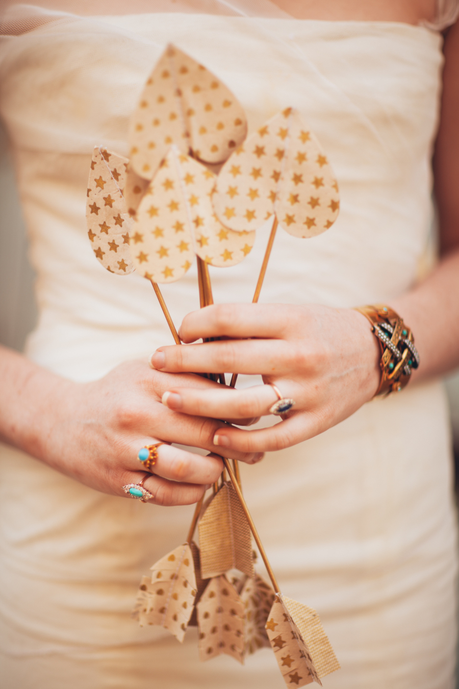 Bride in wedding gown holding gold arrows with turqouise rings.