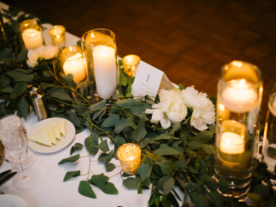 River Roast venue neutral wedding reception head table in white and gold with pillar candles, lush peonies, and eucalyptus garland. 