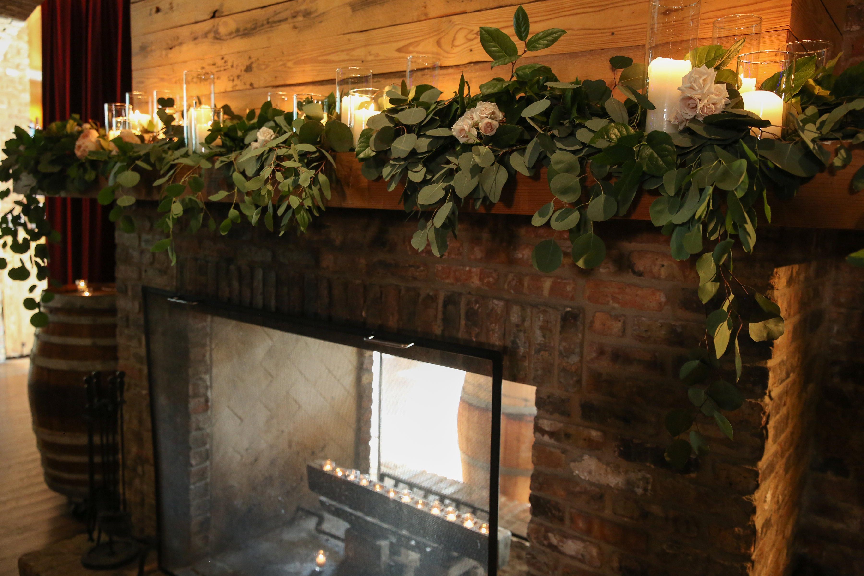 Early summer wedding ceremony rustic fire place mantal with foliage, white majolica, and pillar candles