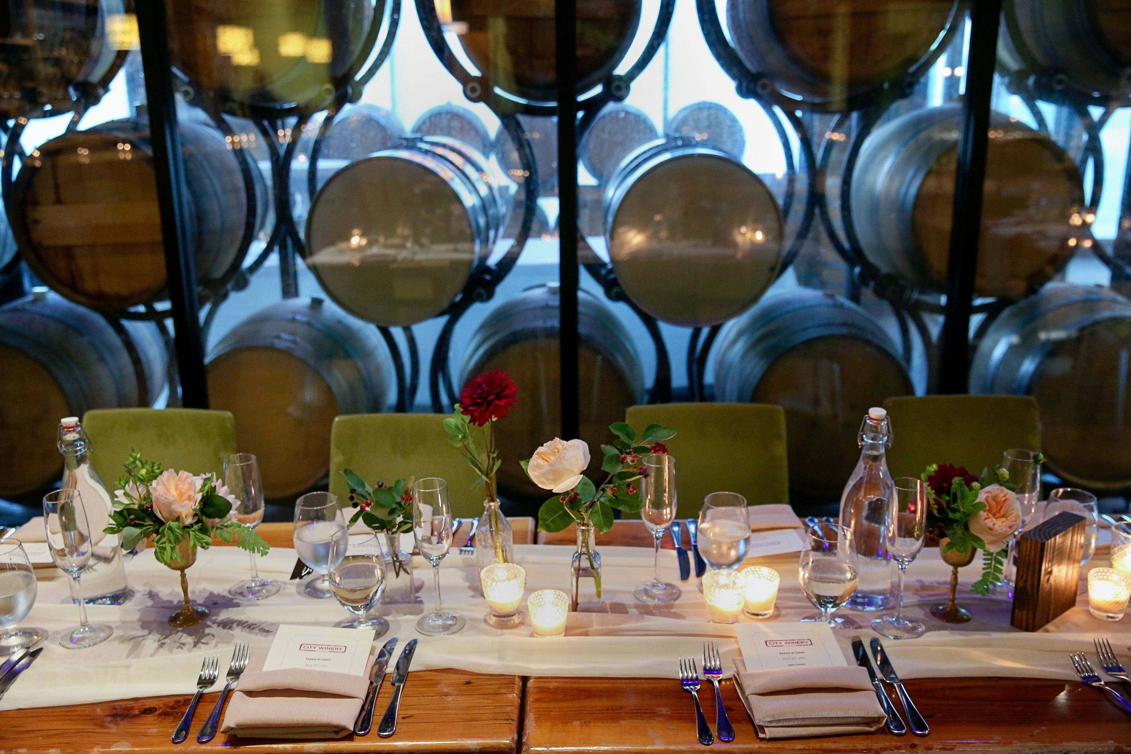 Simple low table arrangements in glass bottles and vintage brass with garden roses and dahlias at winery.
