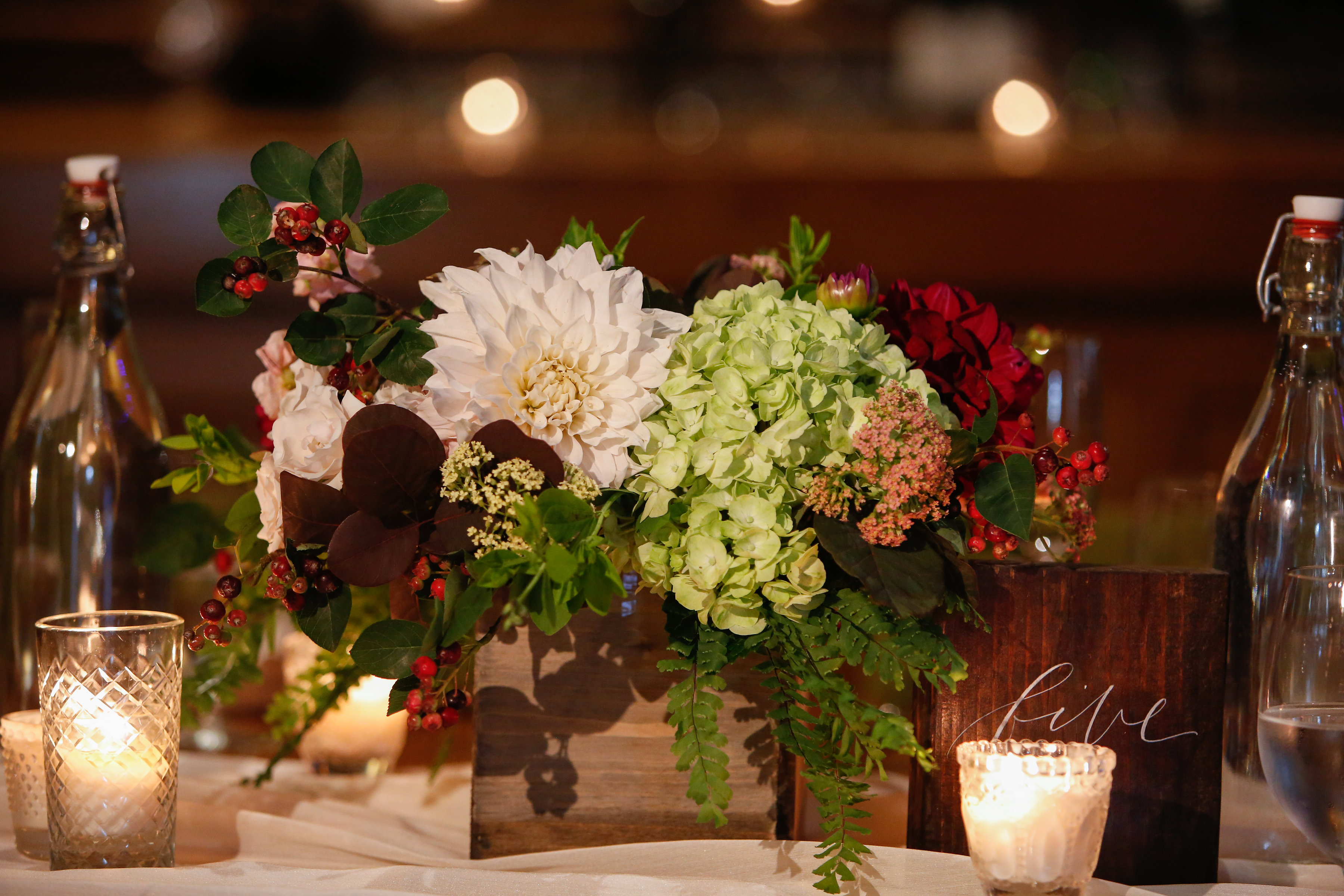 Summer wedding reception arrangement with ivory and burgundy dahlias, green hydangea, berries, and ferns.