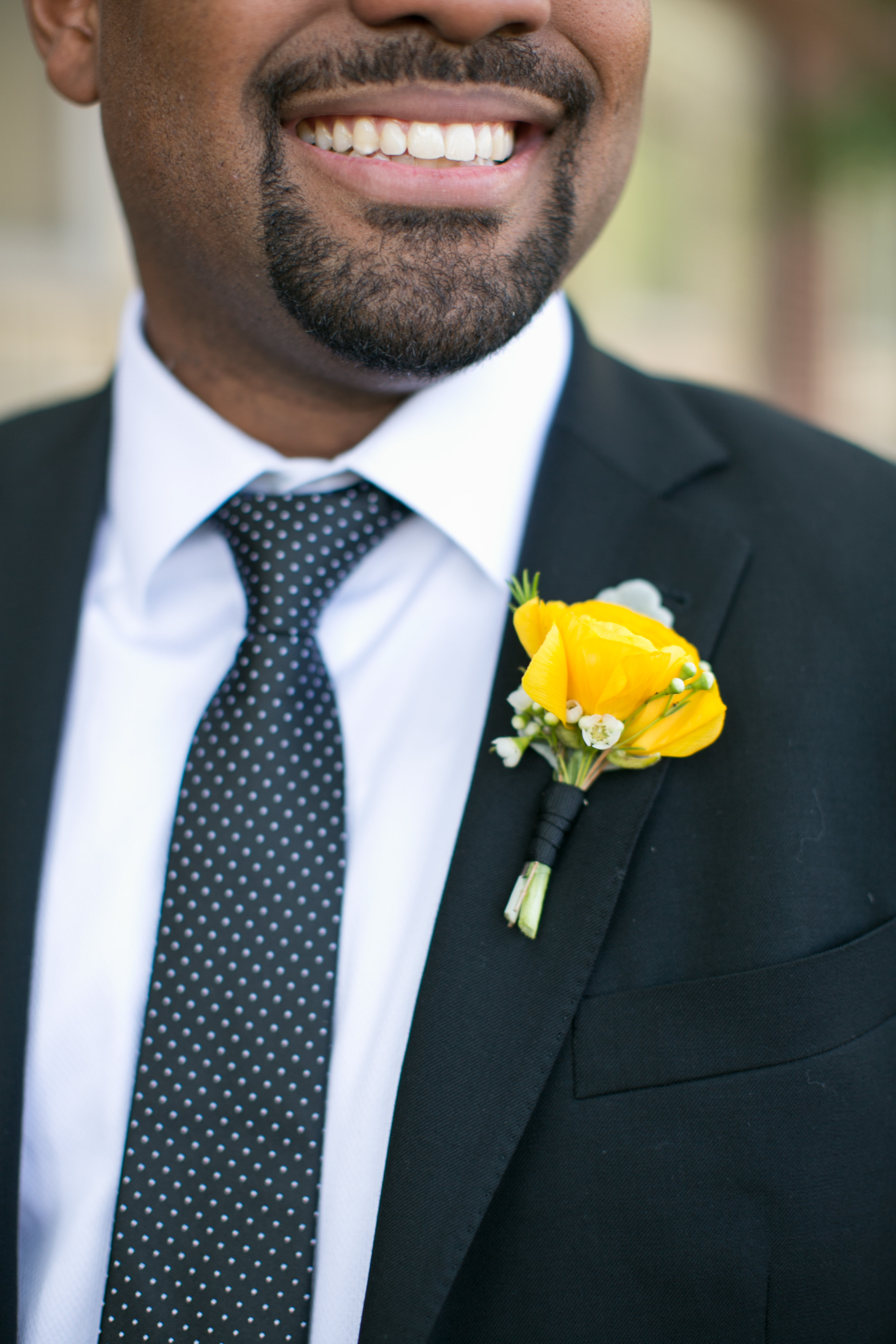 Smiling groom with bright yellow boutonniere and patterned navy tie for summer wedding.