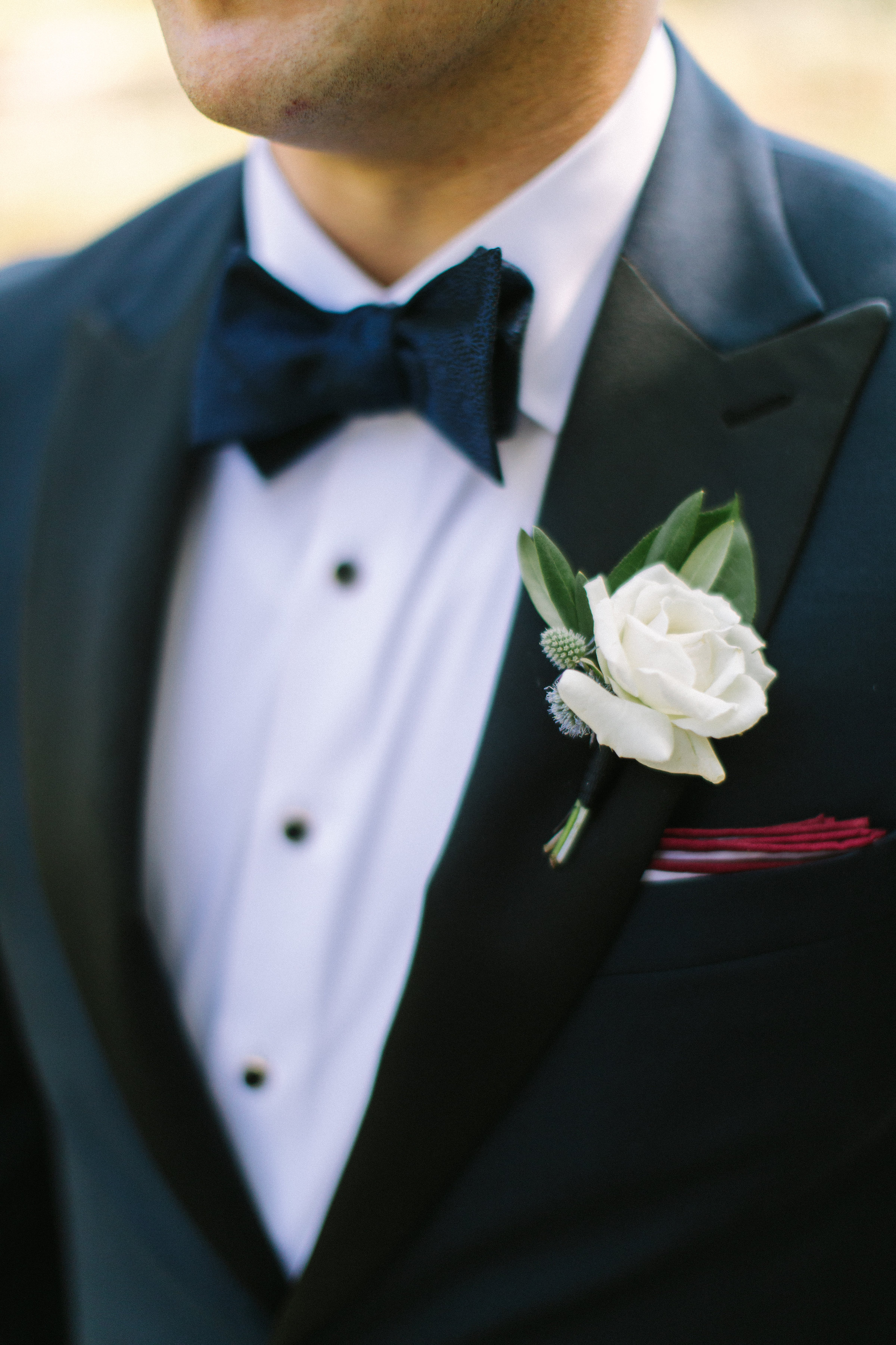 Groom with classic white rose boutonniere with ruby pocket square and bowtie.
