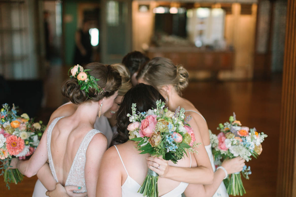 Bridesmaids gathered with colorful garden summer bouquets in pink, ivory, orange, and blue.