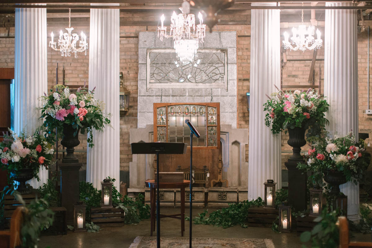 Lush, romantic wedding altar with oversized urns, chandeliers. pillar candles, and foliage.