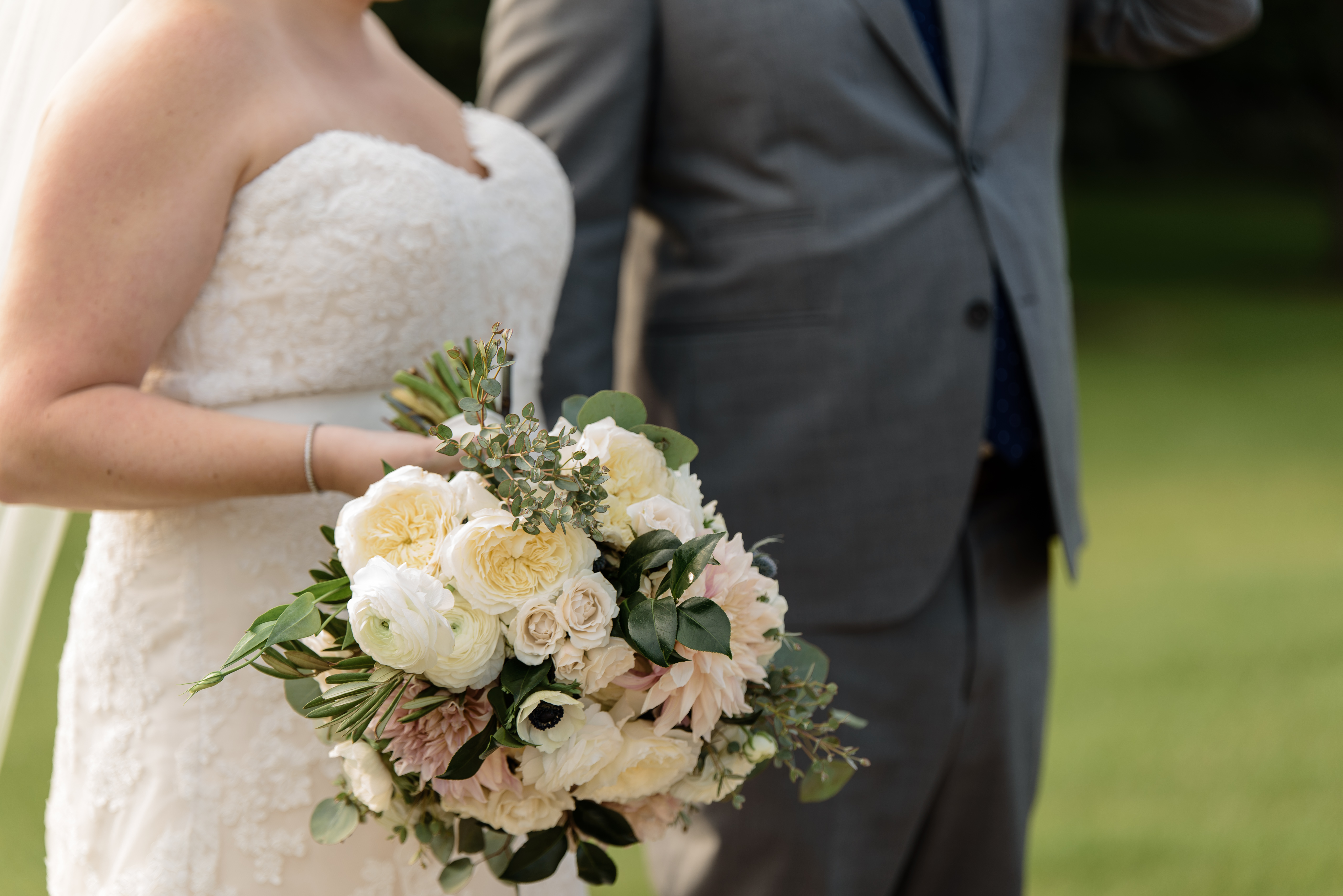 Bride and groom walking with bouquet of ranunculus, garden roses, and dahlias