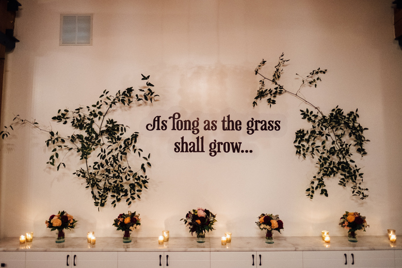 Brique wedding in Chicago. Wall installation with quote surrounded by foliage, with wedding party bouquets..