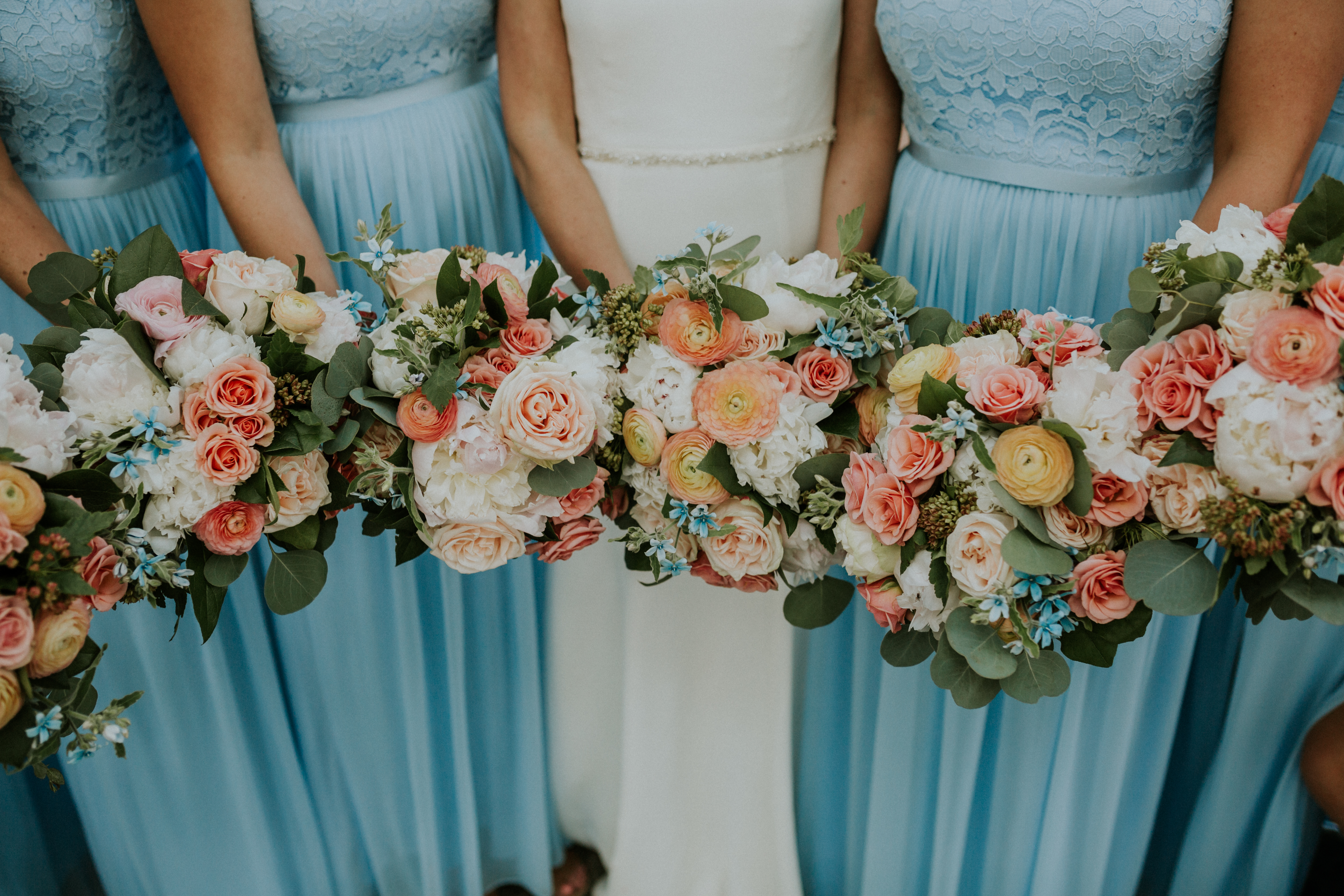 Bridal party in sky blue dresses with gardeny wedding bouquets of roses, peonies, and ranunculus.