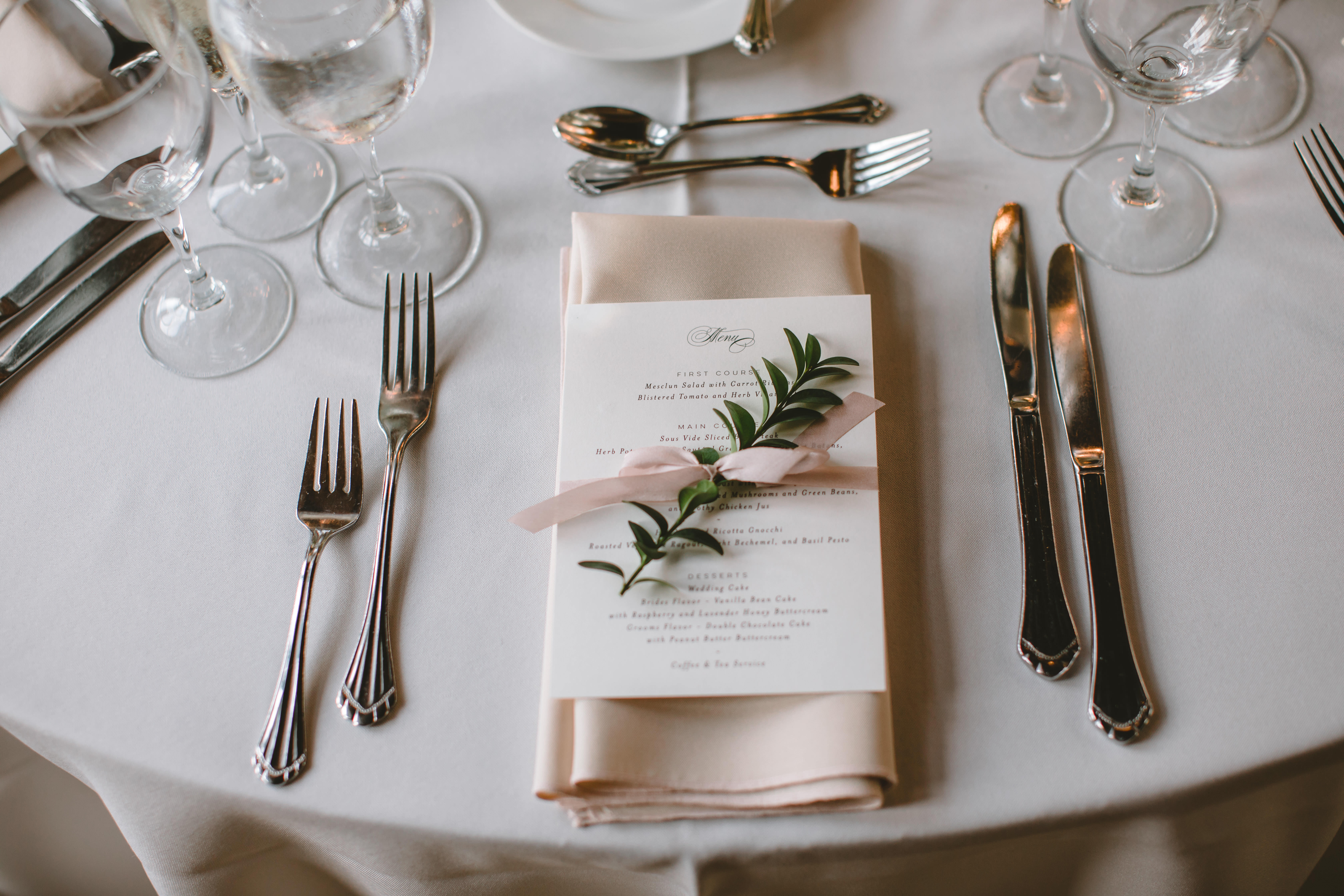 Place setting with taupe linen, blush napkin, menu tied with silk ribbon and boxwood spring.