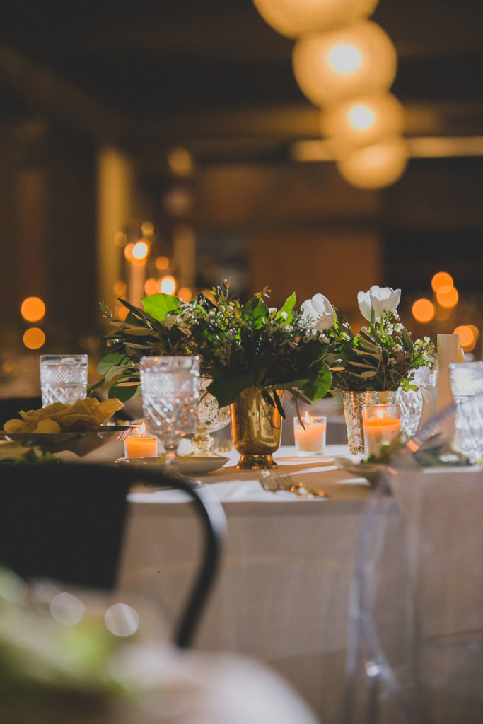 Winter wedding reception at Architectural Artifacts, with green and white arrangements of tulips, ferns, and wax flowers in brass vases.
