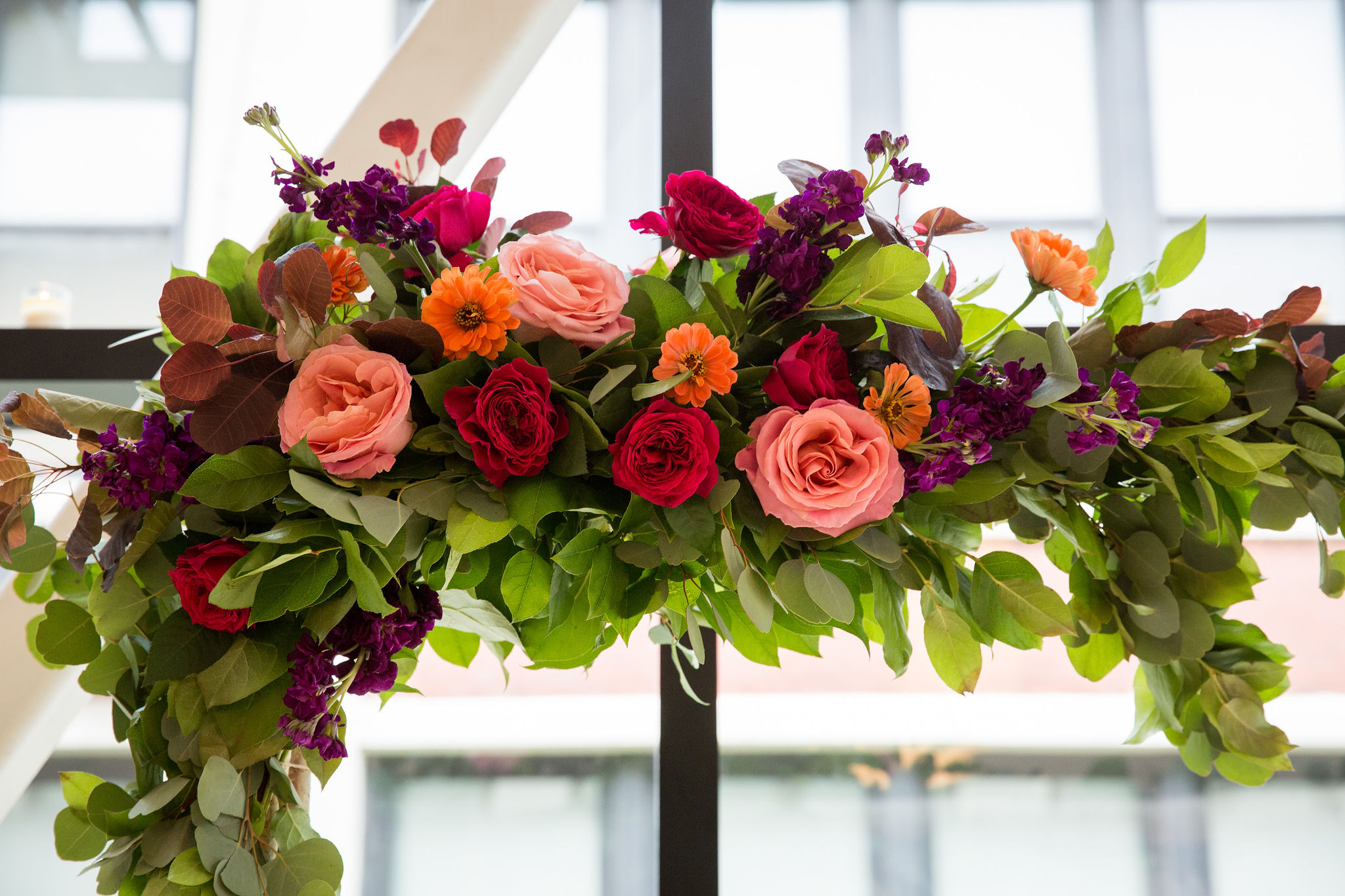 Greenhouse Loft bright summer wedding ceremony altar with colorful arrangement of pink garden roses, orange zinnias, and purple stock.