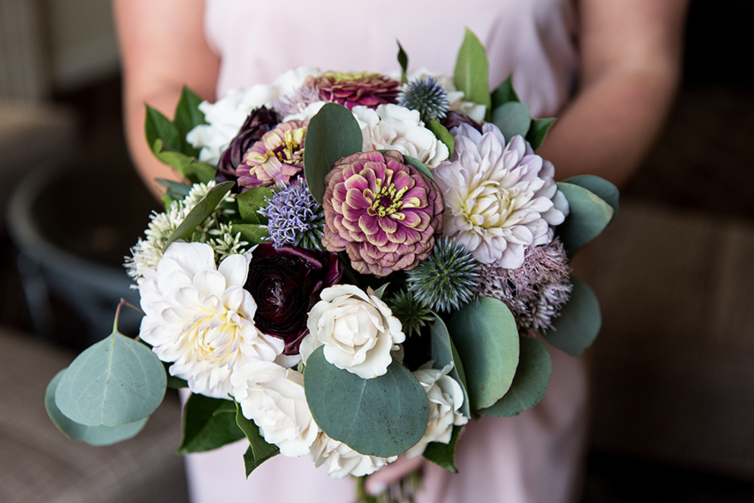 Summer wedding bridal bouquet with pink zinnias, ivory dahlias, plum ranunculus, and eucalyptus.