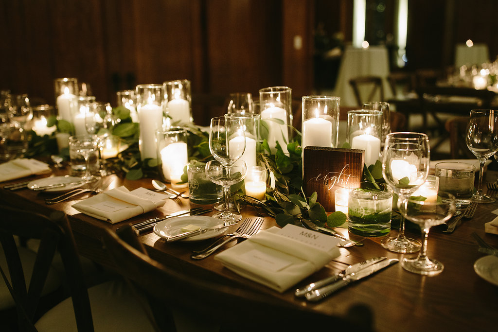 Romantic winter wedding reception at Chicago Athletic Association with white and green table settings of pillar candles and sprawing foliage.