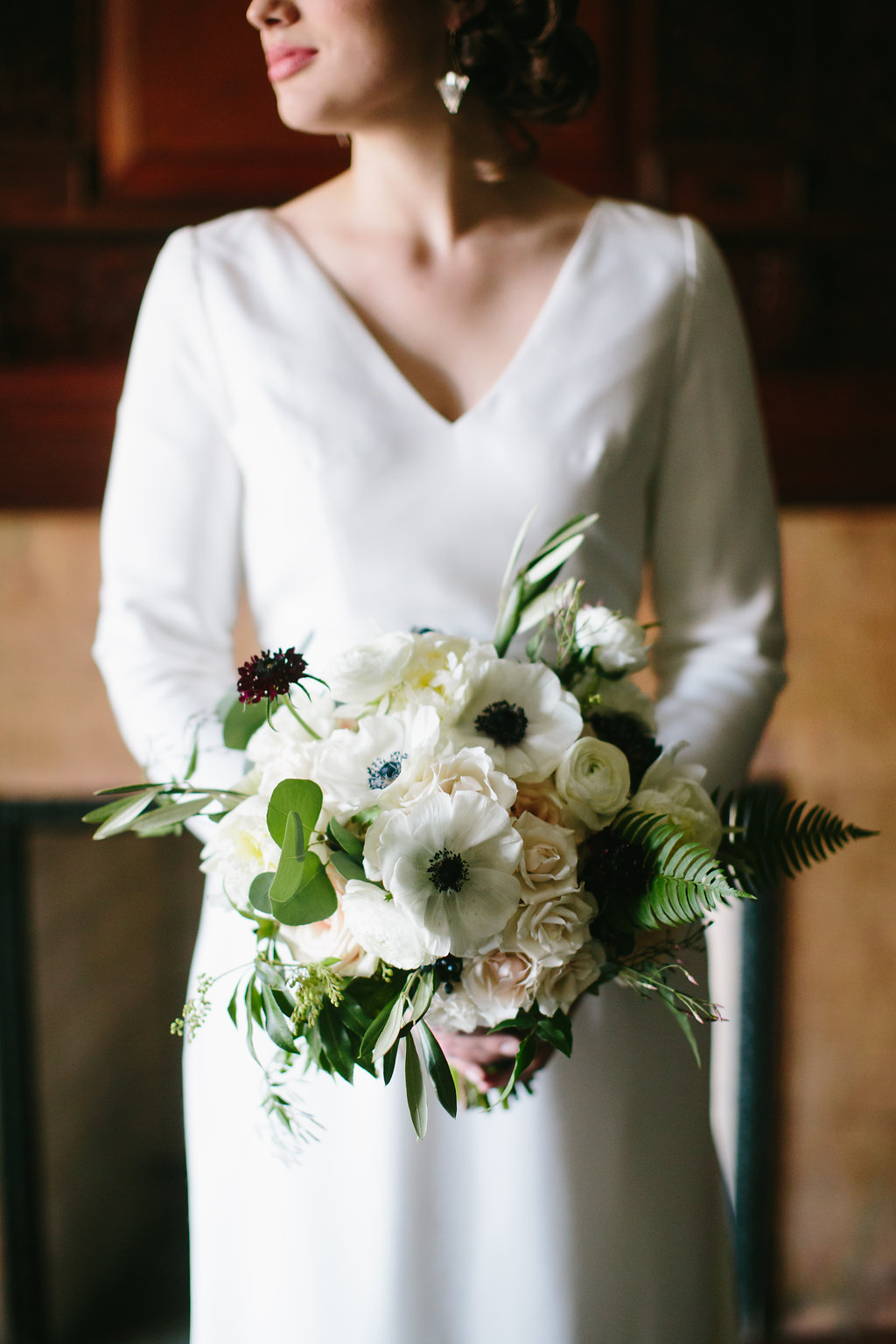 Winter bride with gardeny bouquet of white anemones, blush spray roses, jasmine, fern, and ranunculus.