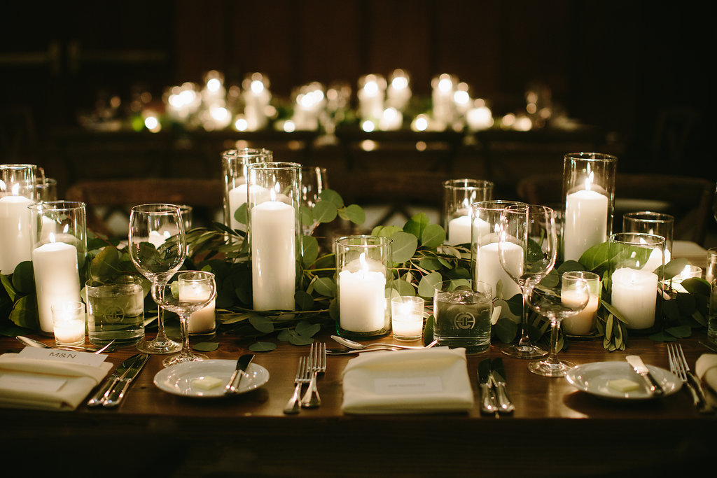 Romantic winter wedding reception at Chicago Athletic Association with white and green table settings of pillar candles and sprawing foliage.