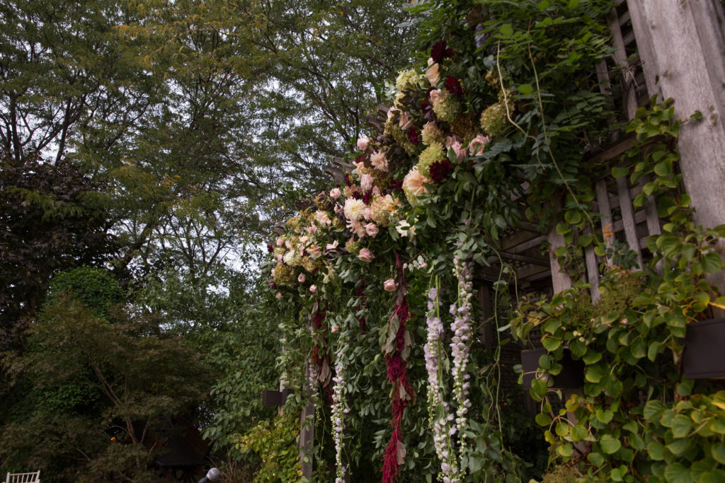 Hanging flower ceremony altar for outdoor fall wedding with garden roses, hydrangea, and burgundy and ivory dahlias.