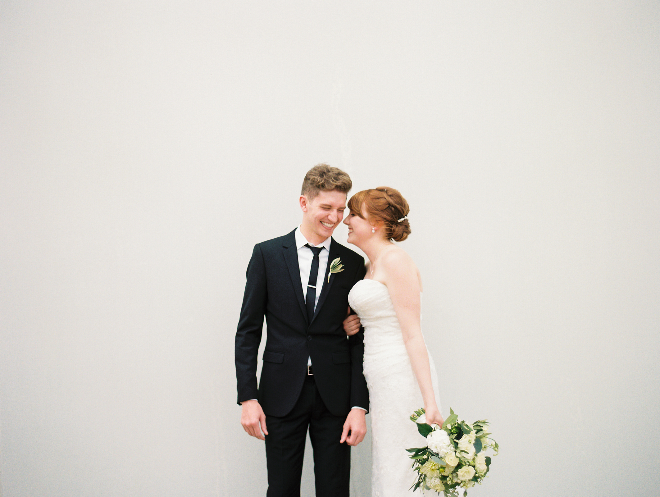 Smiling bride and groom, minimalist monochromatic white wedding with eucalyptus, dahlias, garden roses. 