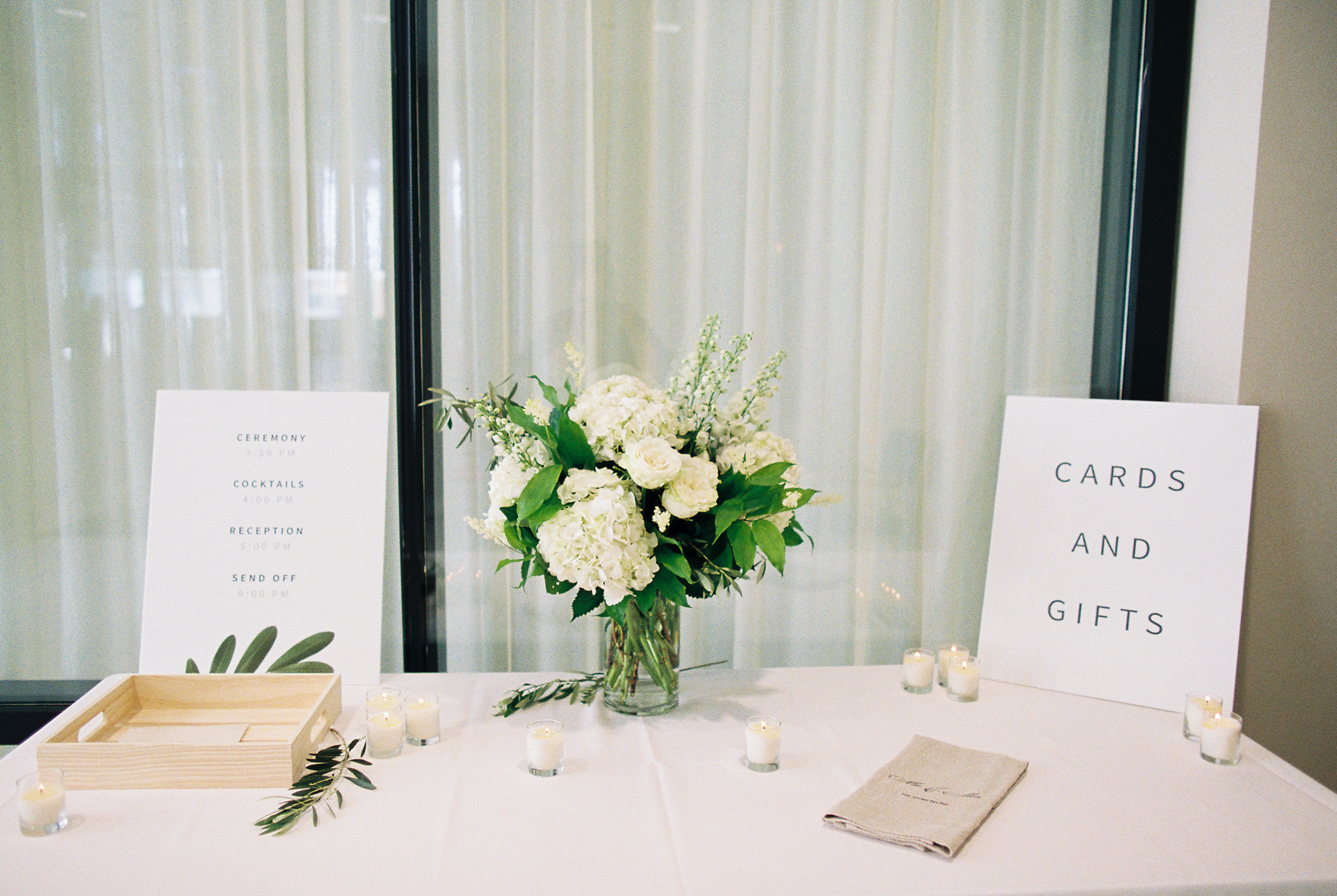 Cards and gifts table for white and green wedding at Greenhouse Loft with candles and arrangement of white hydrangea, garden roses, and eucalyptus.