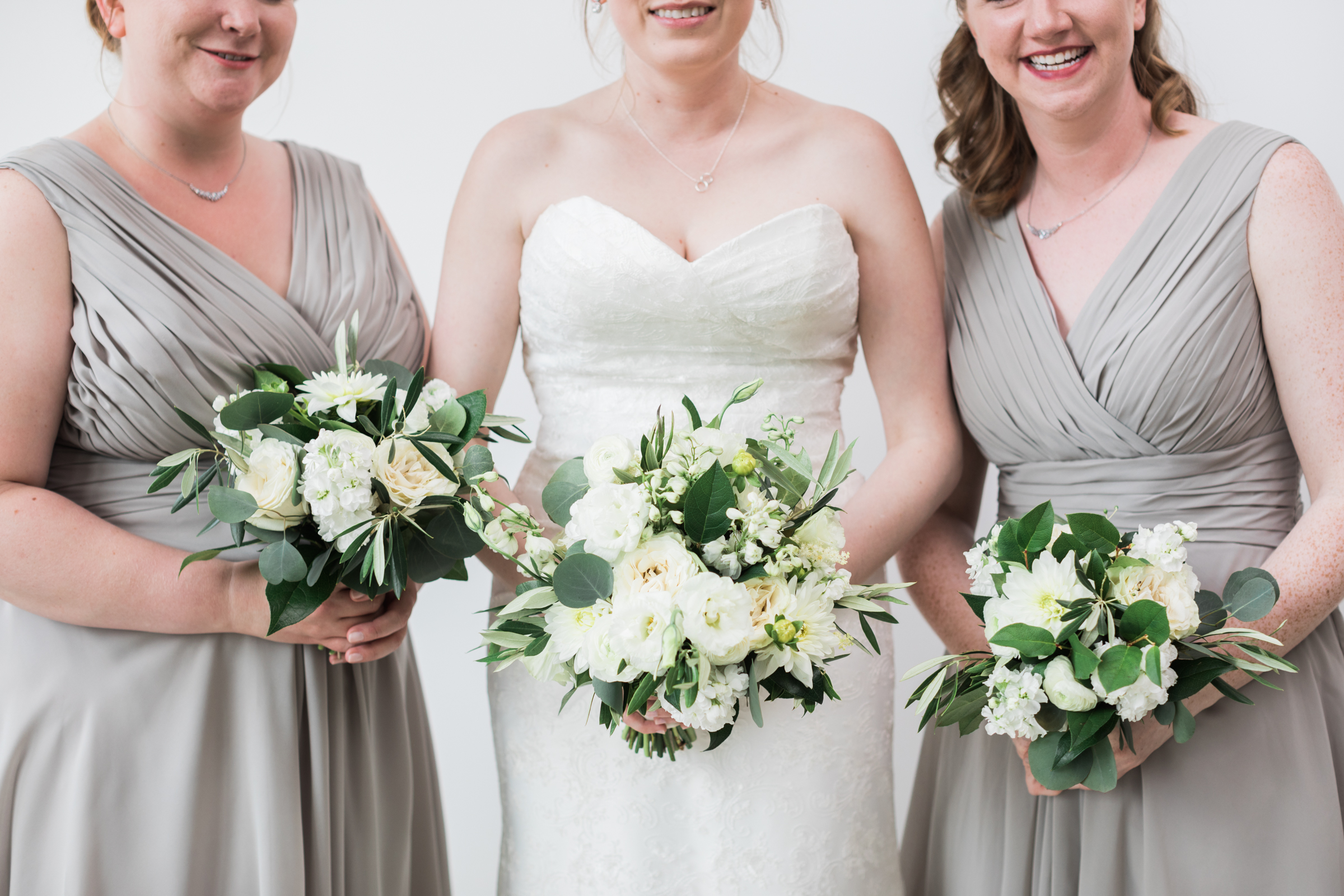 Bride and bridesmaids in pale grey dresses for minimalist monochromatic wedding with white dahlias, ranunculus, roses, and eucalyptus.