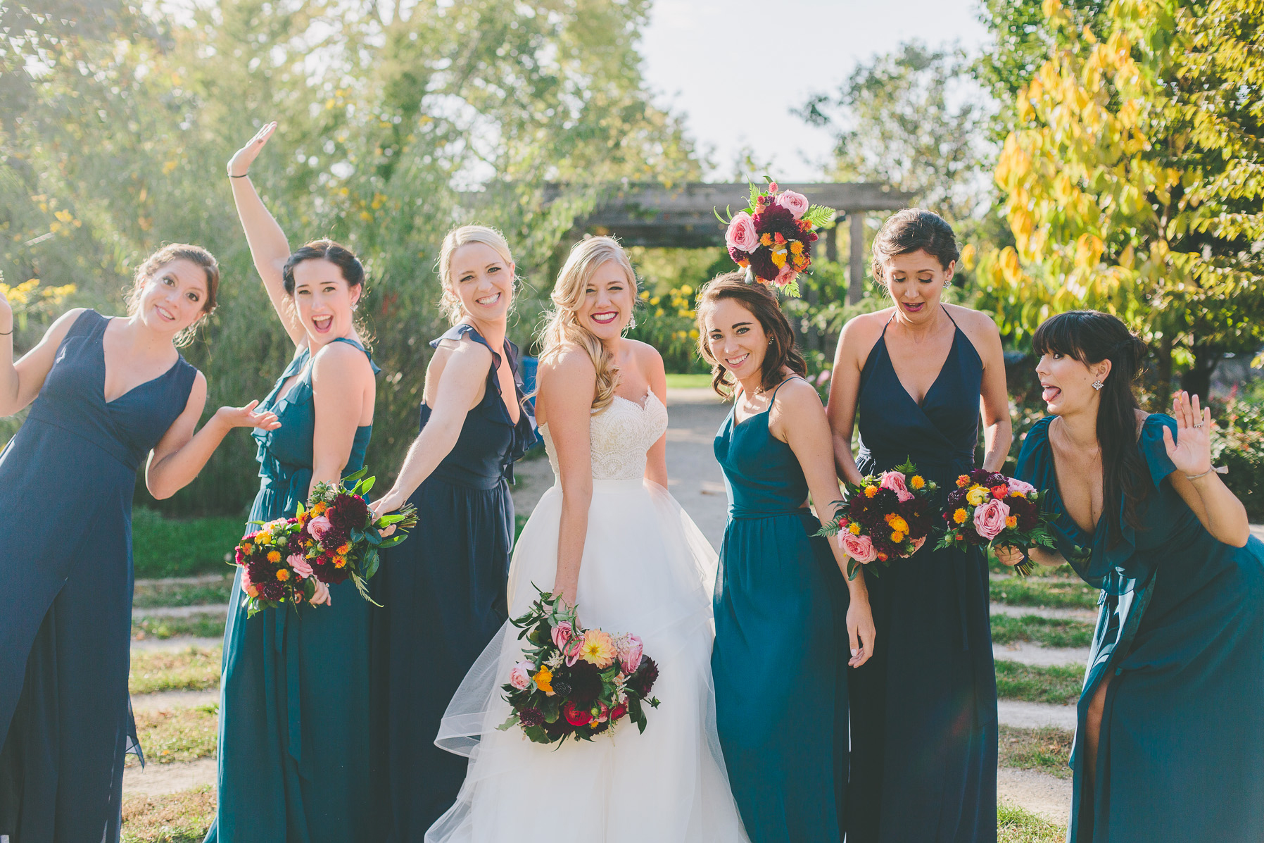 Fall wedding bridal party outside with teal dresses and bouquet with pink roses, plum scabiosa and dahlias, red and bright yellow ranunculus.