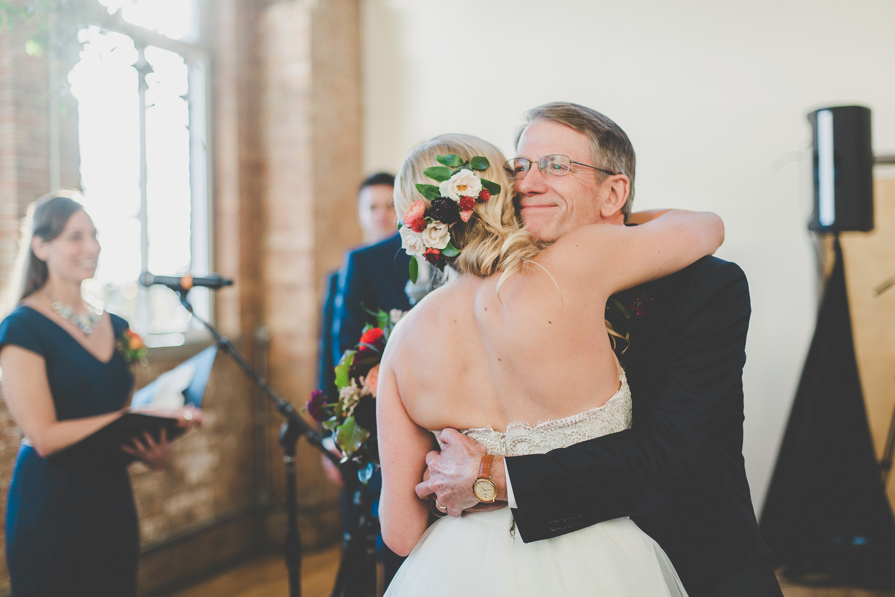 Bride hugging father with flower hair piece in pink, plum, red, and ivory. 