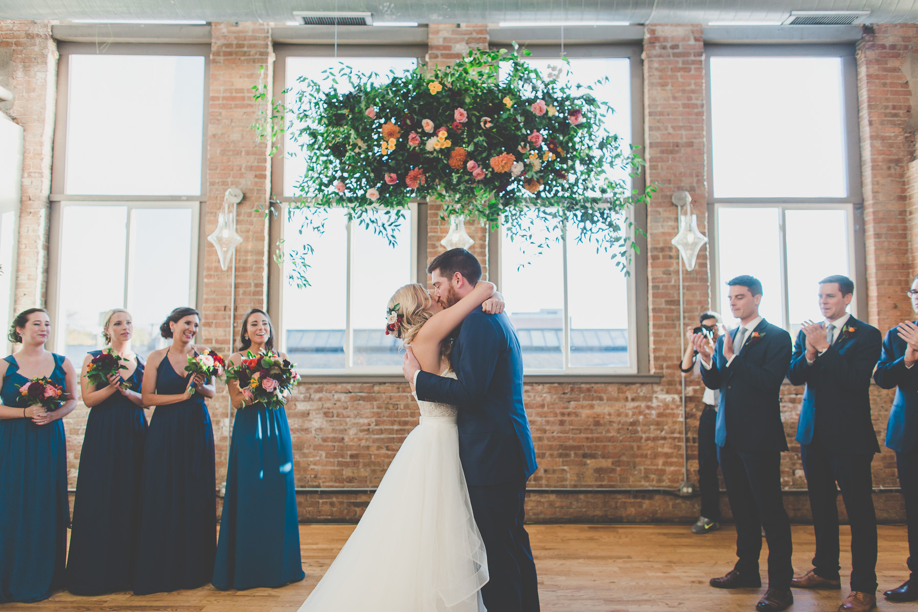 Bride and groom kissing fall wedding with floating flower ceremonial altar of pink garden roses, yellow lisianthus, orange dahlias, and foliage.