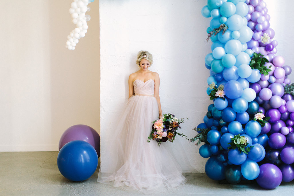 Bride with playful blue ceremony backdrop and champagne dress with gardeny bouquet of pink dahlia and peonies, irises, plum scabiosa, hydrangea, berries, tweedia, and lilac.