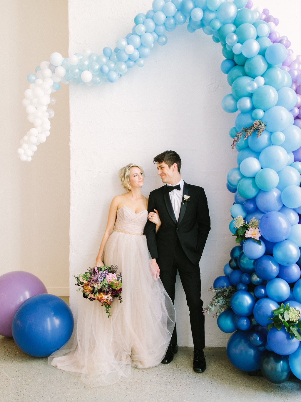 Bride and groom with playful blue ceremony backdrop and champagne dress with gardeny bouquet of pink dahlia and peonies, irises, plum scabiosa, hydrangea, berries, tweedia, and lilac.