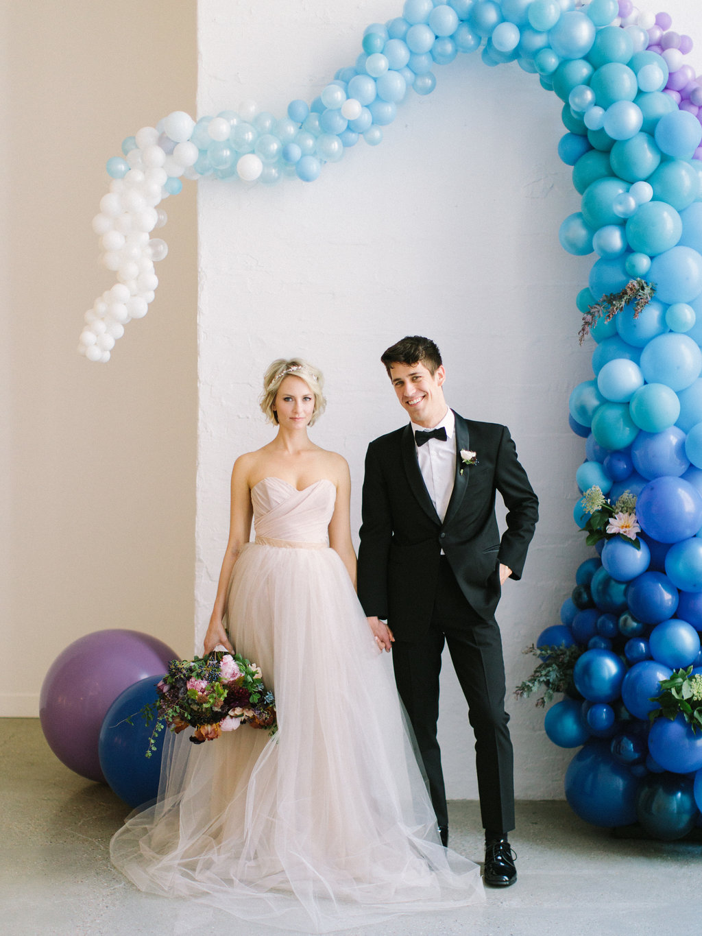 Bride and groom with playful blue ceremony background and champagne dress with gardeny bouquet of pink dahlia and peonies, irises, plum scabiosa, hydrangea, berries, tweedia, and lilac.