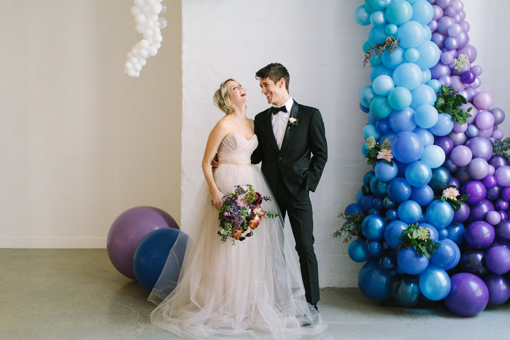 Bride and groom with playful blue ceremony backdrop and champagne dress with gardeny bouquet of pink dahlia and peonies, irises, plum scabiosa, hydrangea, berries, tweedia, and lilac.