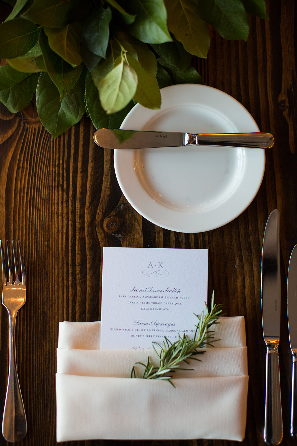 Wedding place setting with rosemary sprig in napkin with menu.