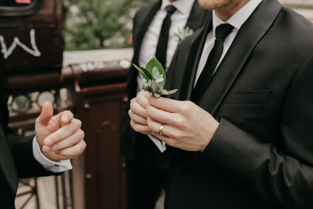 Man holding boutonniere of green foliage for a spring wedding.