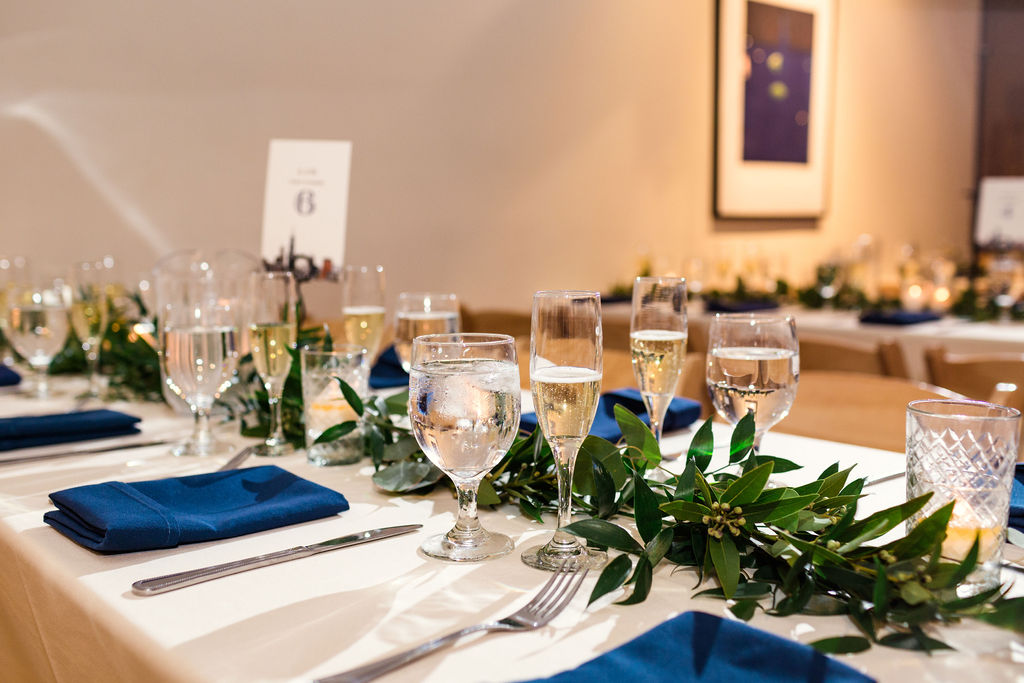 Simply elegant reception at Floating World Gallery with linens of white and blue and foliage garlands and votives lining the tables.