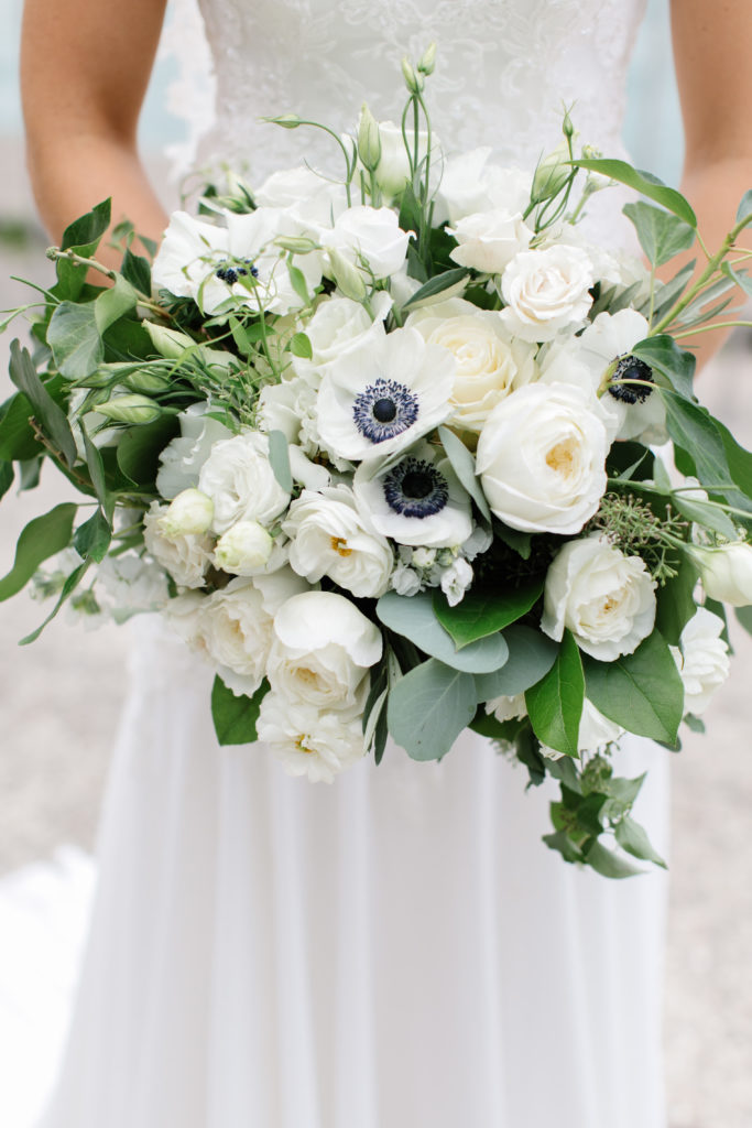 Bridal bouquet of white garden roses, lisianthus, anemones, and foliage.