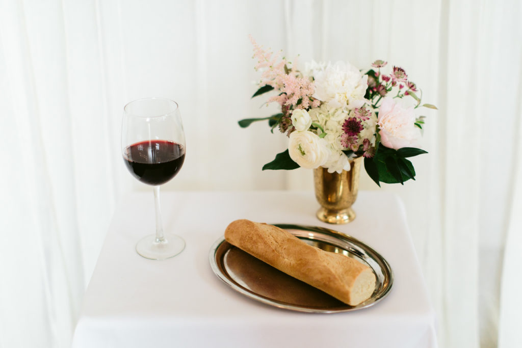 Communion bread and wine table for this couple's spring wedding ceremony, featuring a small arrangement of ranunculus, peonies, and astilbe.