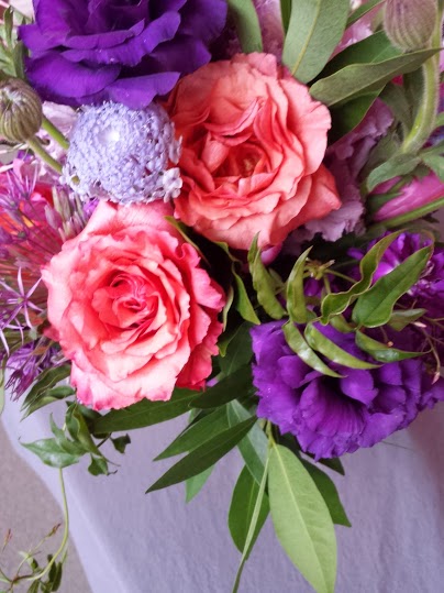Bouquet in purple, orange, and pink, with Dark Milva roses, purple lisianthus, scabiosa, allium, and jasmine.
