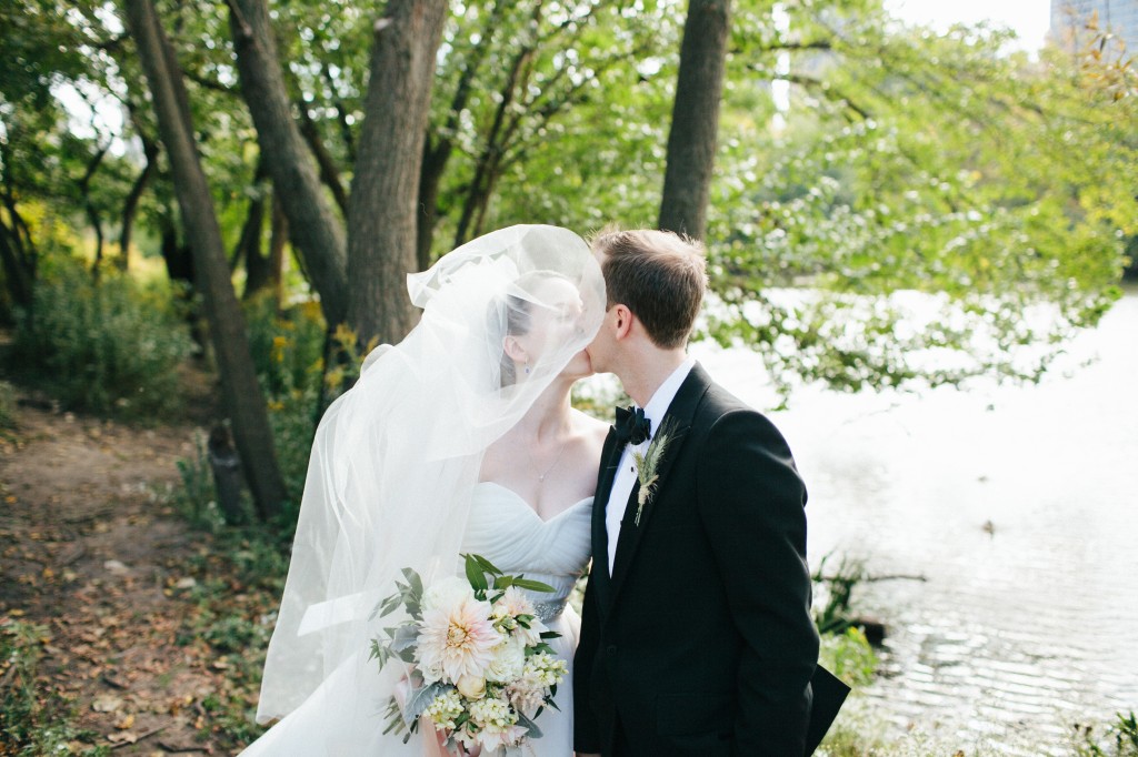 Bride and groom kissing outdoors under windswept veil.