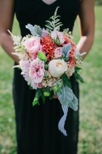 Bridesmaid in black dress holding a bouquet in peach, blush, coral, and grey.