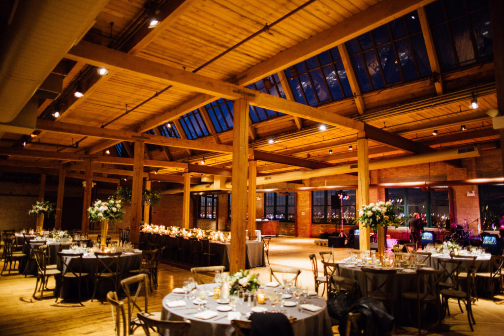 Bridgeport Art Center's Skyline Loft in Chicago wedding reception with rustic tables, tall centerpieces with ivory garden roses in gold vases. 