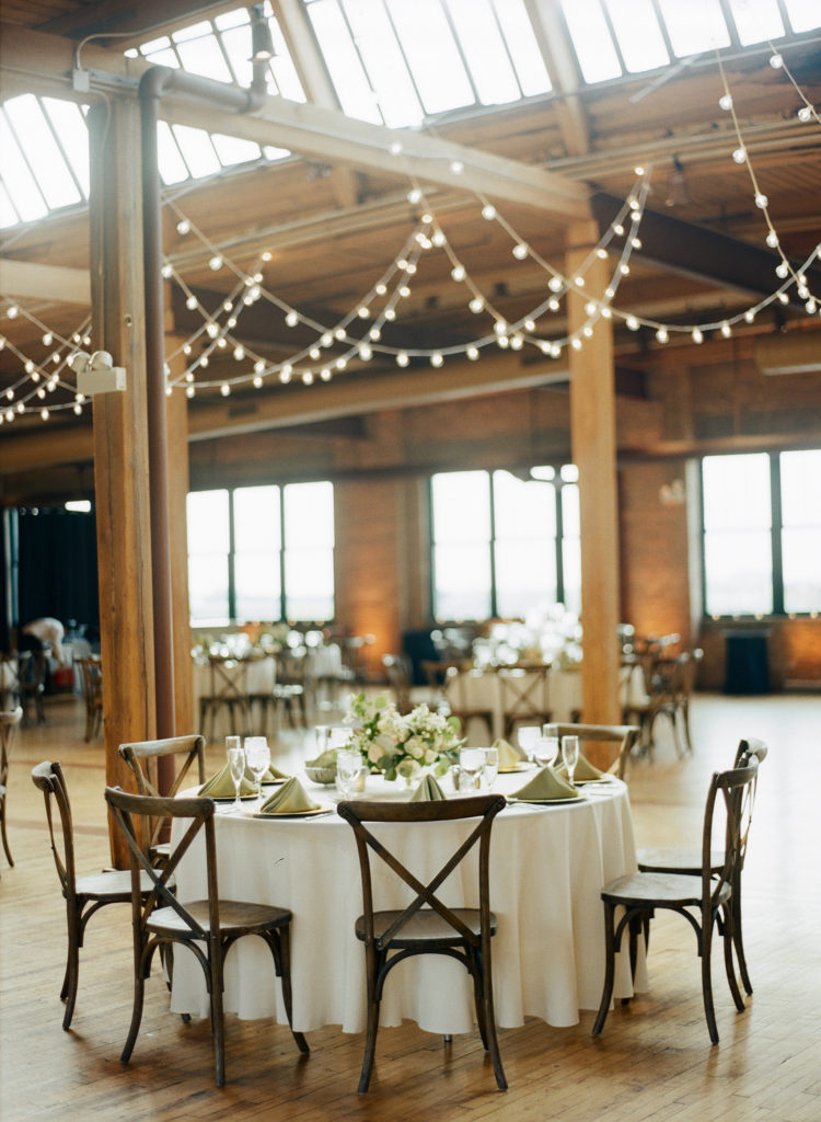 Bridgeport Art Center's Skyline Loft in Chicago wedding reception with cafe lights and arrangement with ivory garden roses, stock, and eucalyptus. 