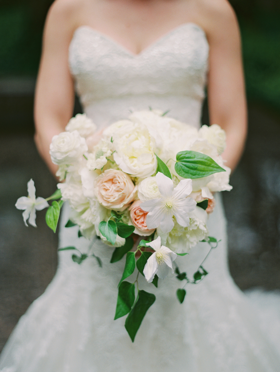 Bride holding bouquet of autumn whit eclematis with vines, blush and cream garden roses and peonies.