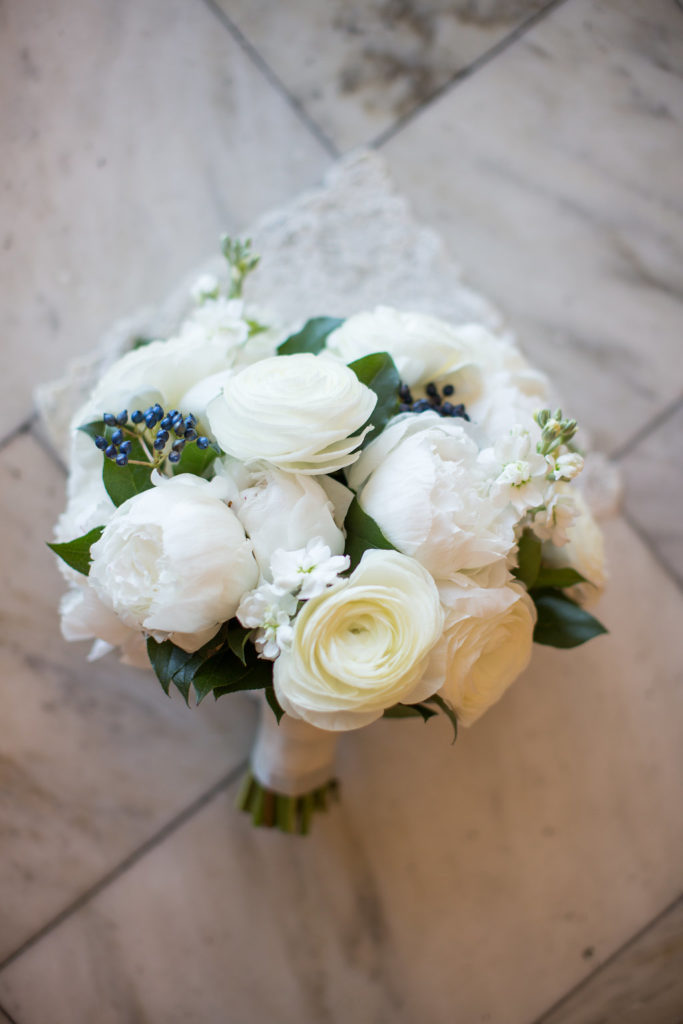 White monochromatic bridal bouquet with full peonies, ranunculus, stock, and navy berries for a romantic spring wedding.