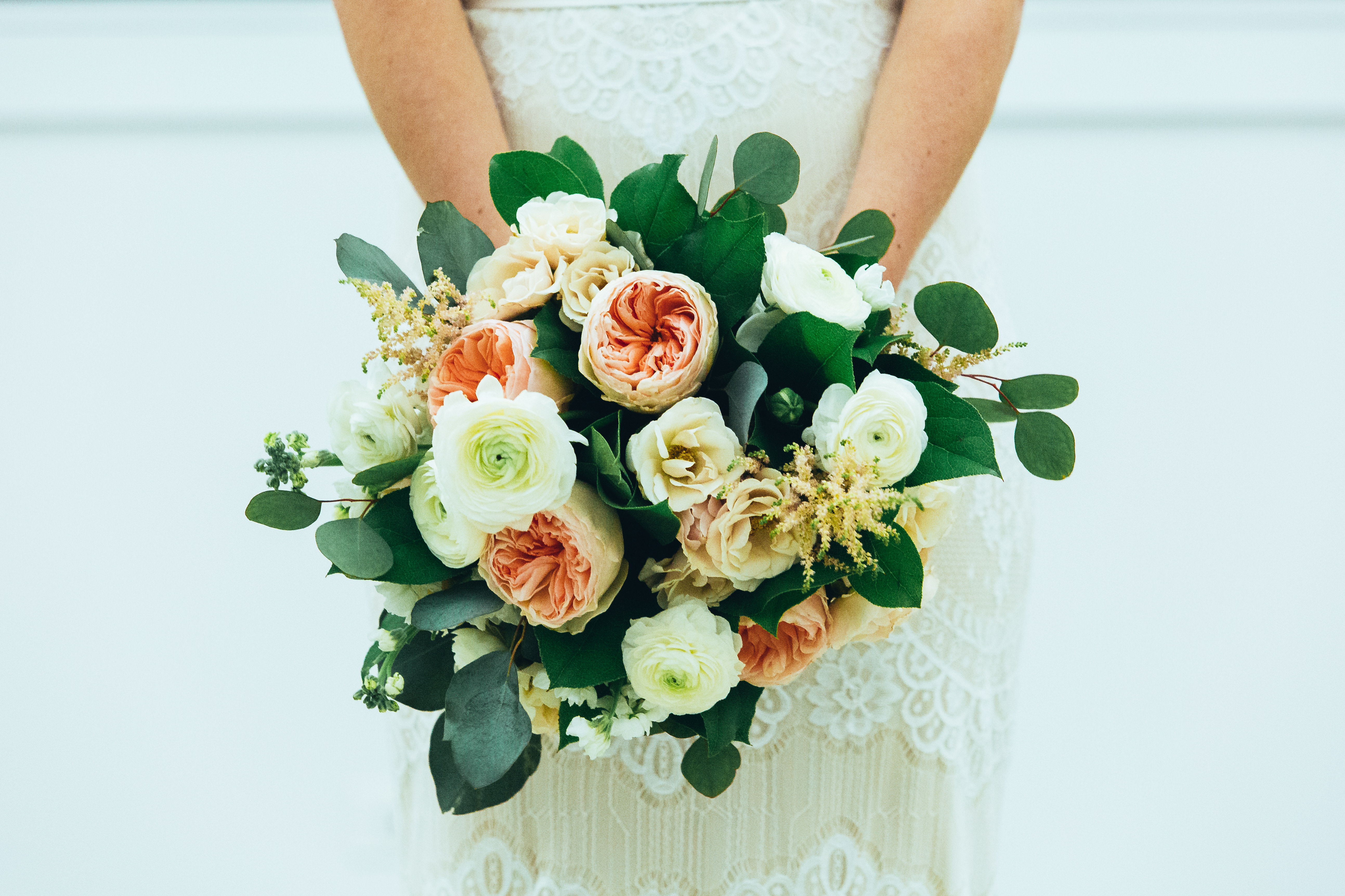 Coral garden roses in bridal bouquet with champagne astilbe, ranunculus, and lisianthus.