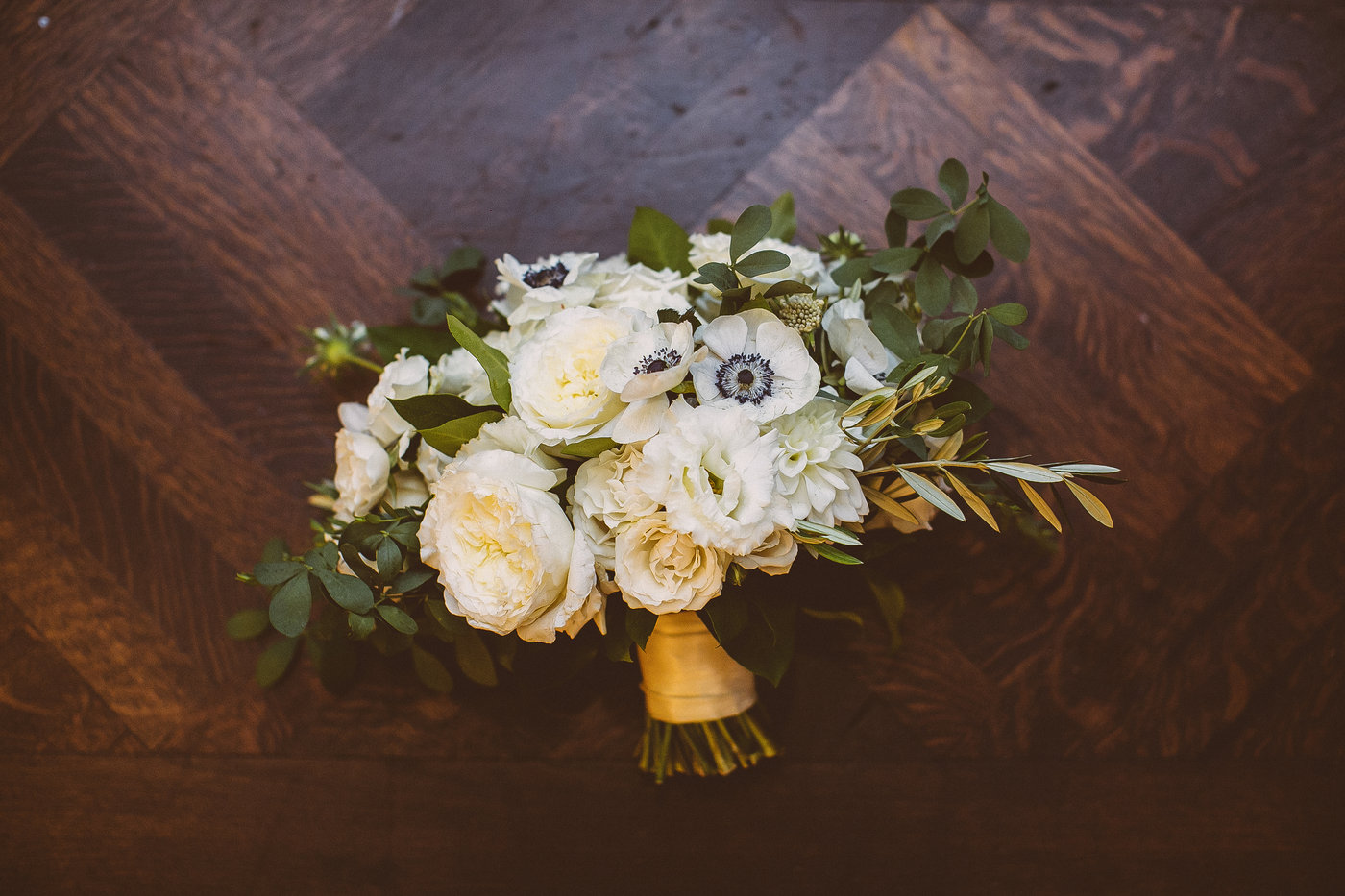 Bride's monochromatic bouquet of garden roses, white anemone, eucalyptus, and lisianthus with gold band.